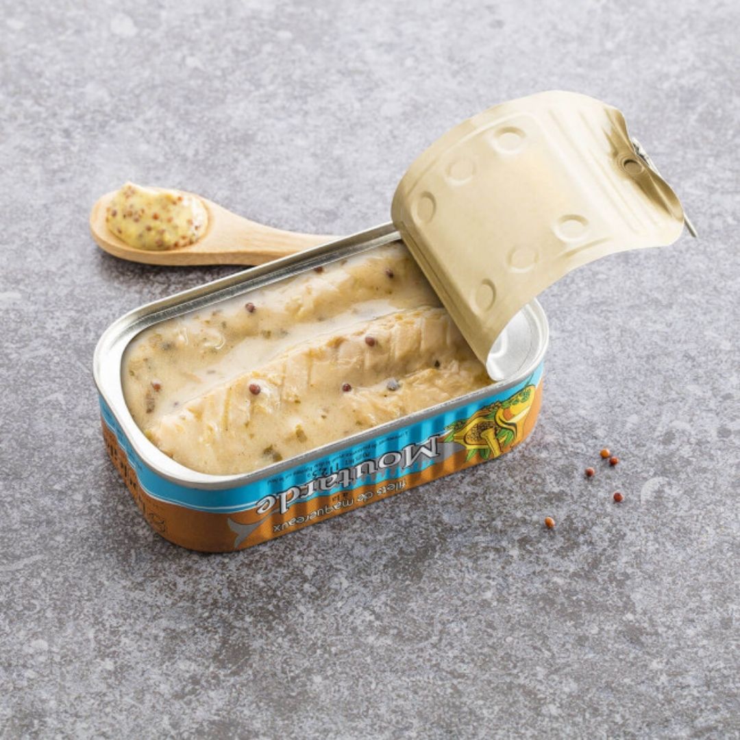 Opened tin showing mackerel fillets submerged in creamy mustard sauce flecked with mustard seeds