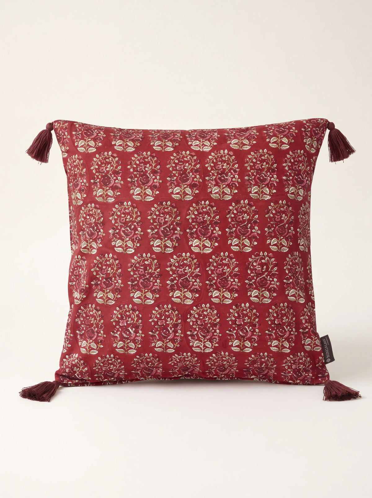 Square ruby red cotton cushion with repeated block-printed floral motifs and corner tassels