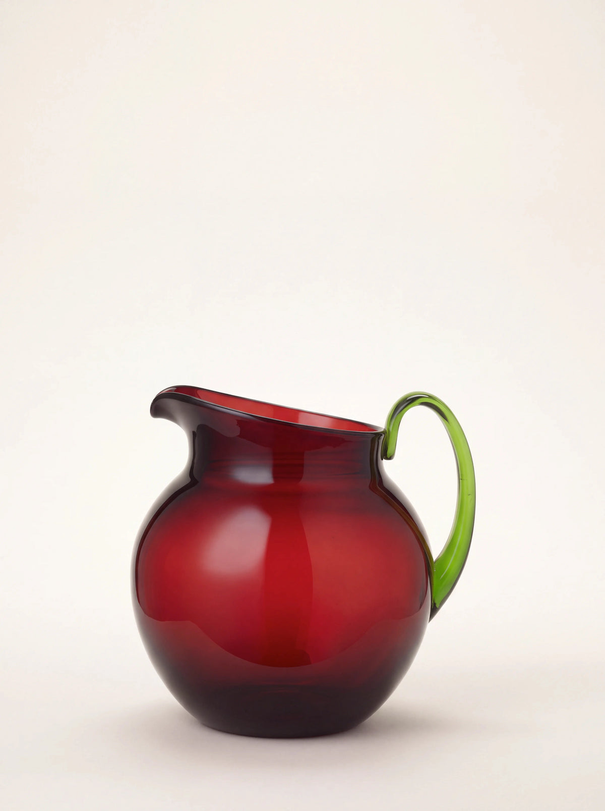 Ruby red acrylic pitcher with a round spherical body, angled spout, and curved green handle