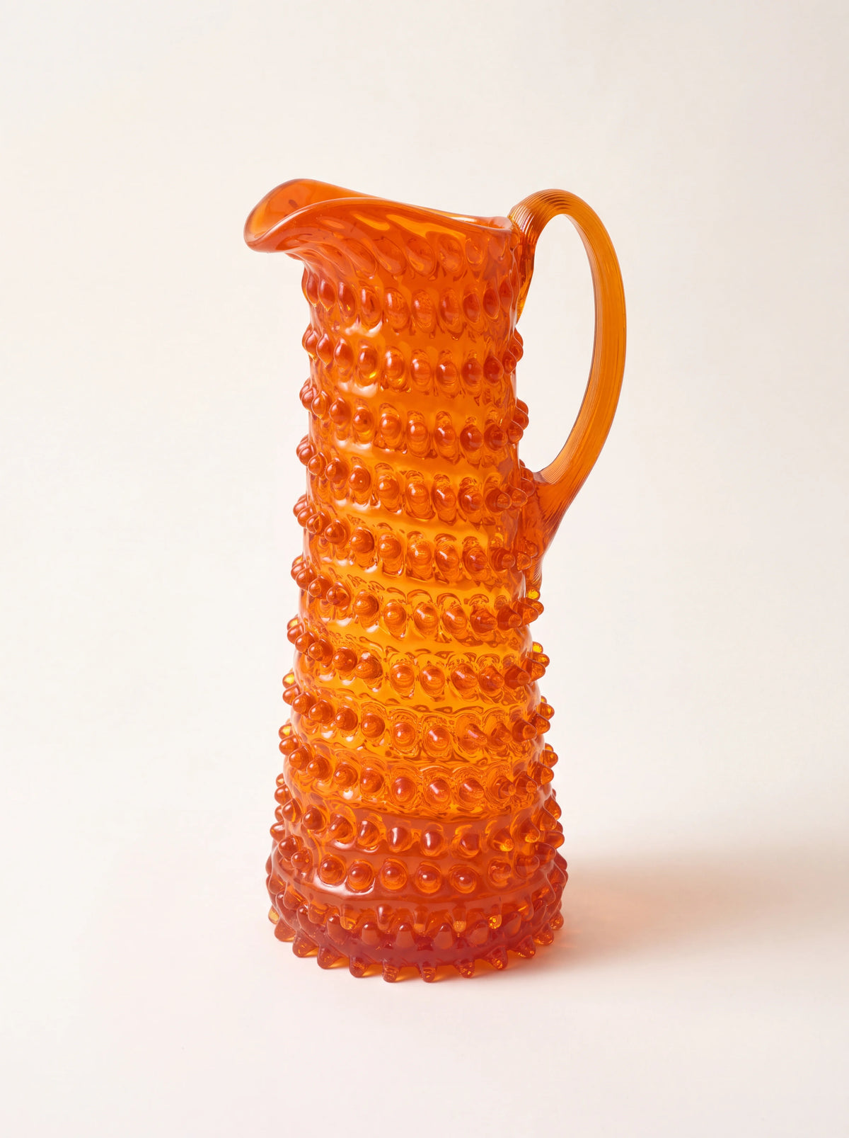 Orange hobnail glass jug with a tapered silhouette, arched handle and pouring spout