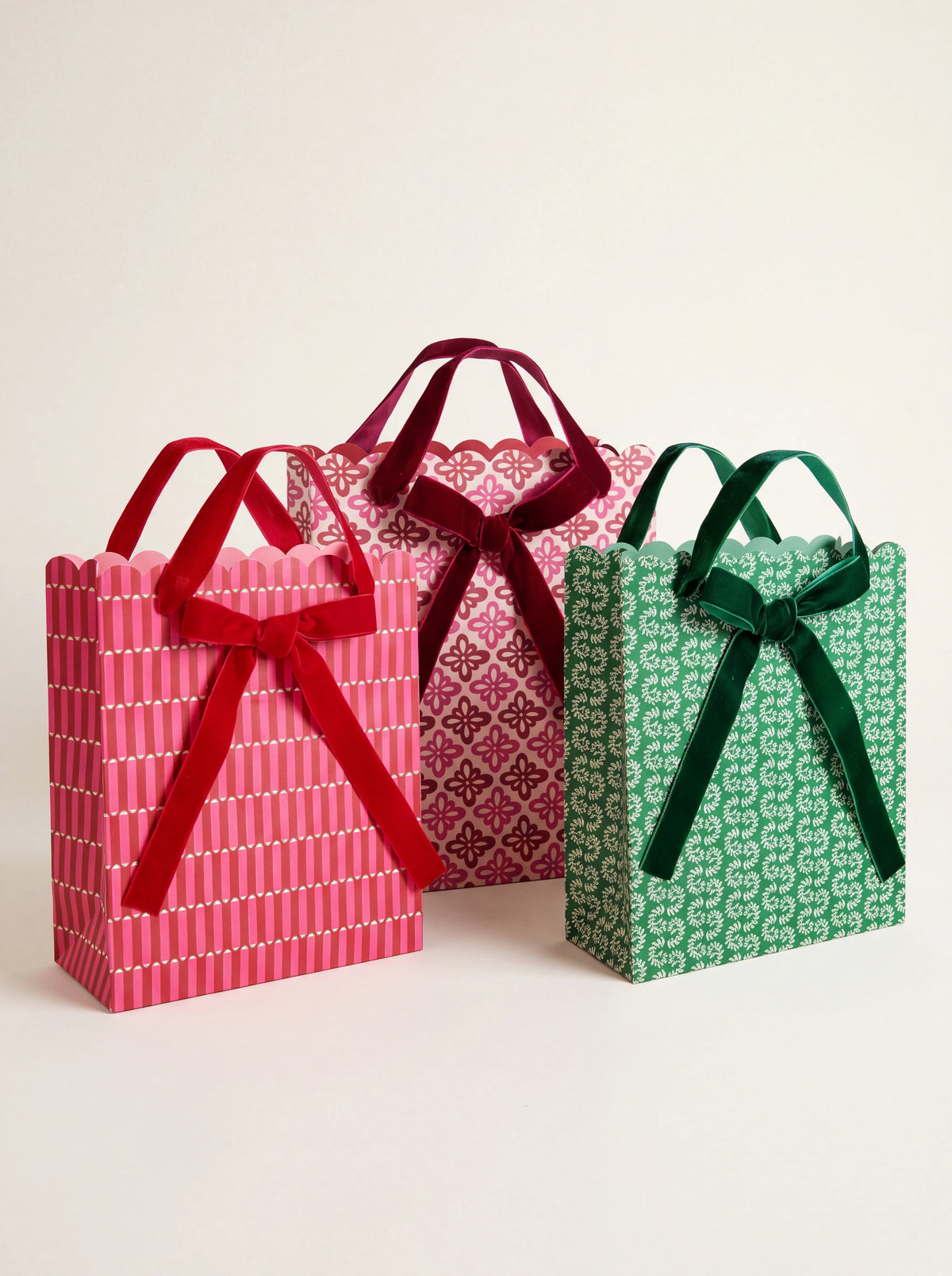 Three block-printed paper gift bags with scalloped edges, velvet ribbon handles, and bows in pink and green