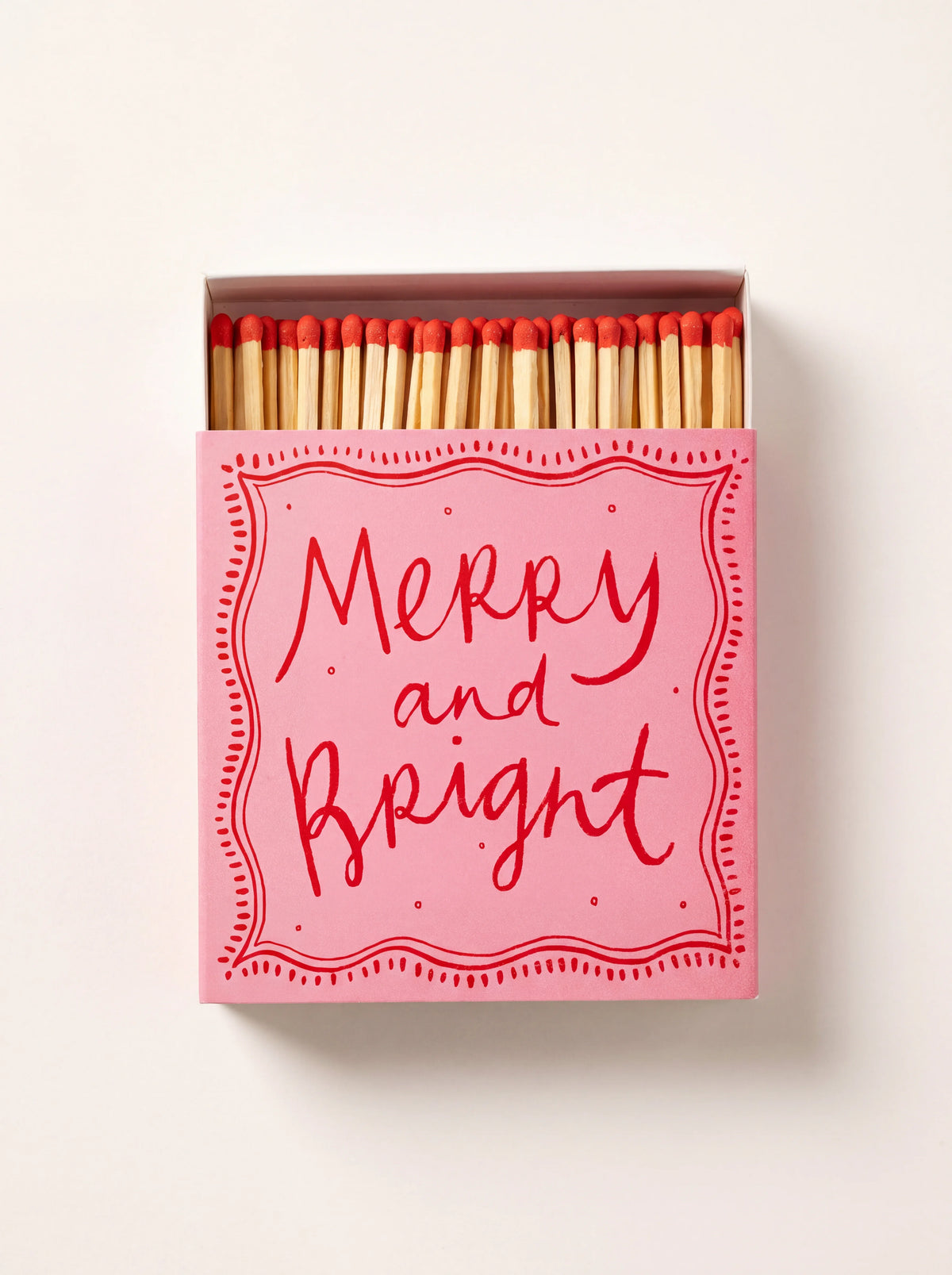Pink sliding matchbox printed with "Merry and Bright", partly opened to reveal red-tipped wooden matches