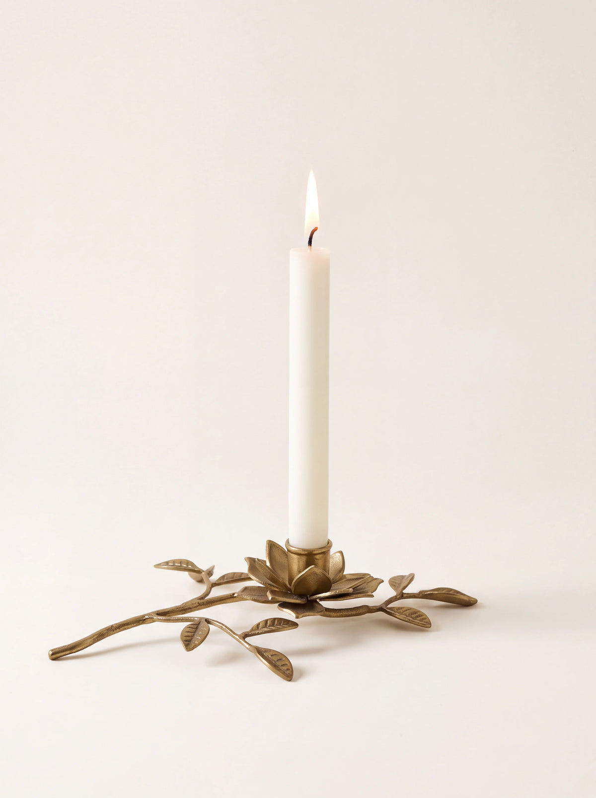 Gold iron branch candle holder holding a single lit white taper candle