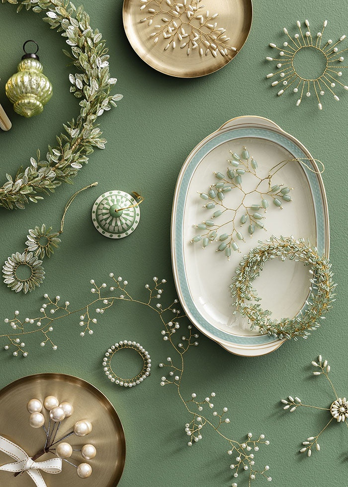 White pearl beaded garland winding across a green surface alongside festive wreaths, dishes and ornaments