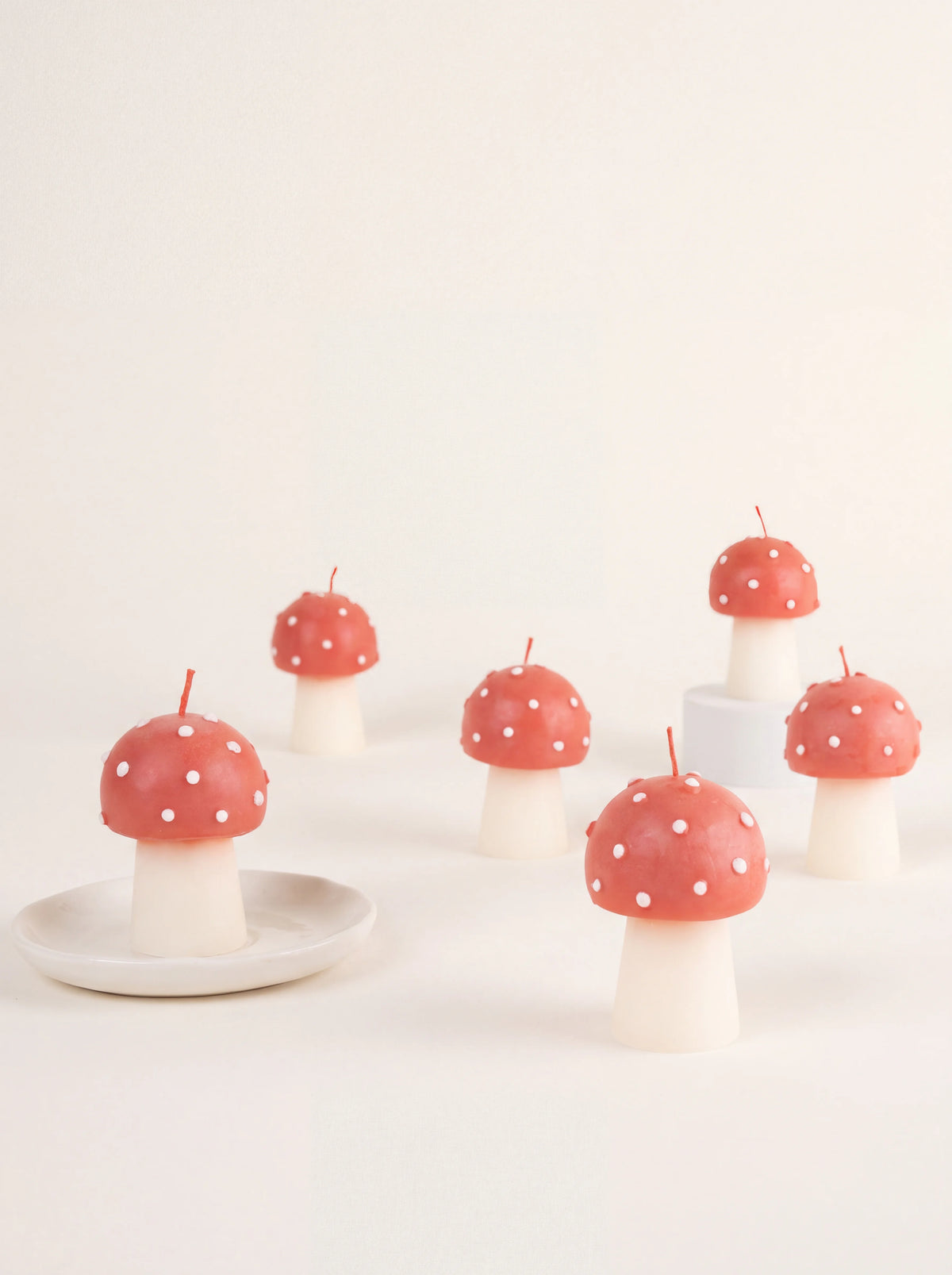 Set of six mini mushroom wax candles with red spotted caps and white stems, one resting on a small dish