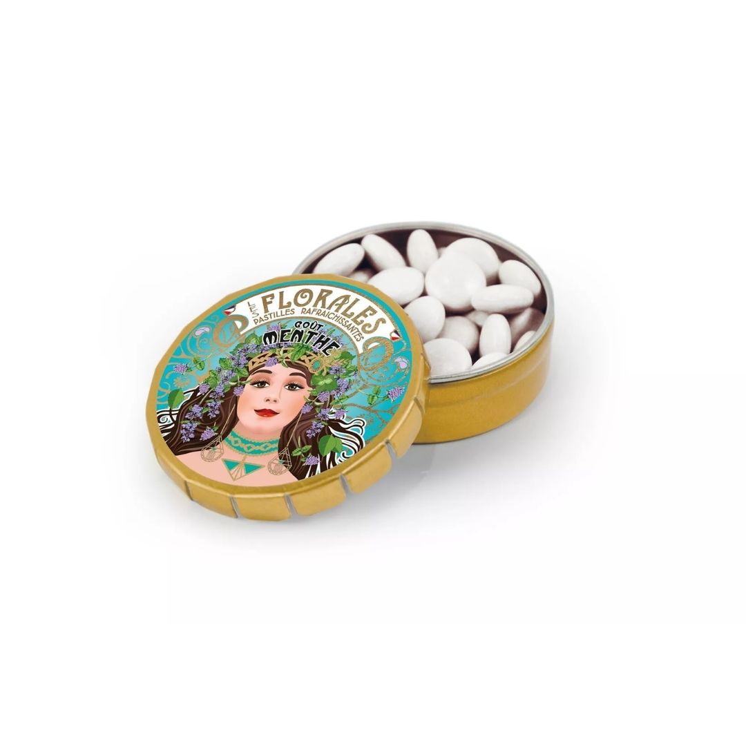 Open gold-tone metal tin filled with small white mint pastilles, lid leaning in front