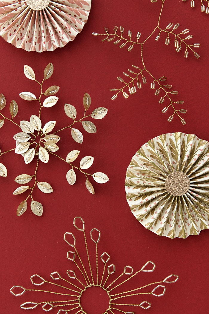 Champagne beaded twig ornament laid flat beside paper rosettes and festive wire decorations
