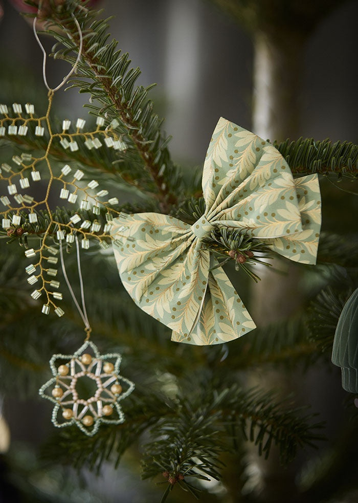 Beaded twig ornament hanging from an evergreen branch beside a patterned paper bow