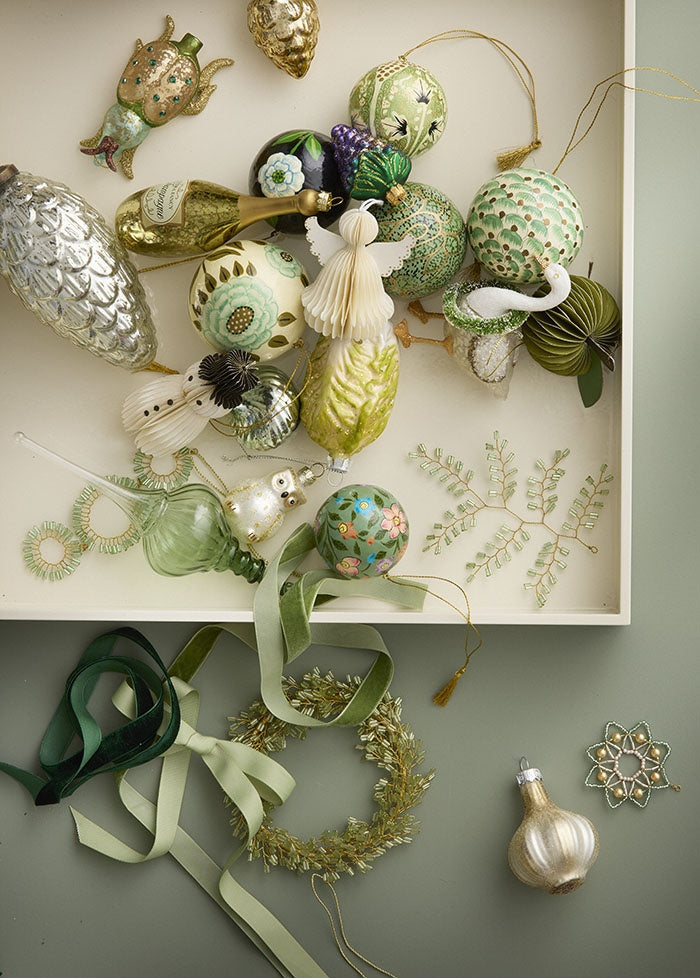 Beaded wreath ornament lying with green velvet ribbons beneath a tray of assorted decorations