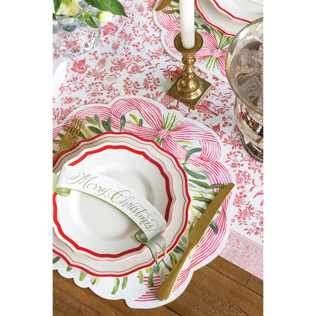 Mistletoe paper placemat layered beneath red-rimmed plates and gold-toned cutlery on a table setting