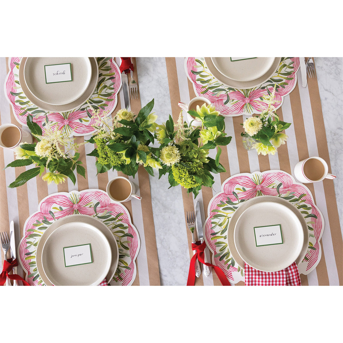 Table setting with four mistletoe paper placemats, ceramic plates, name cards and green floral arrangements
