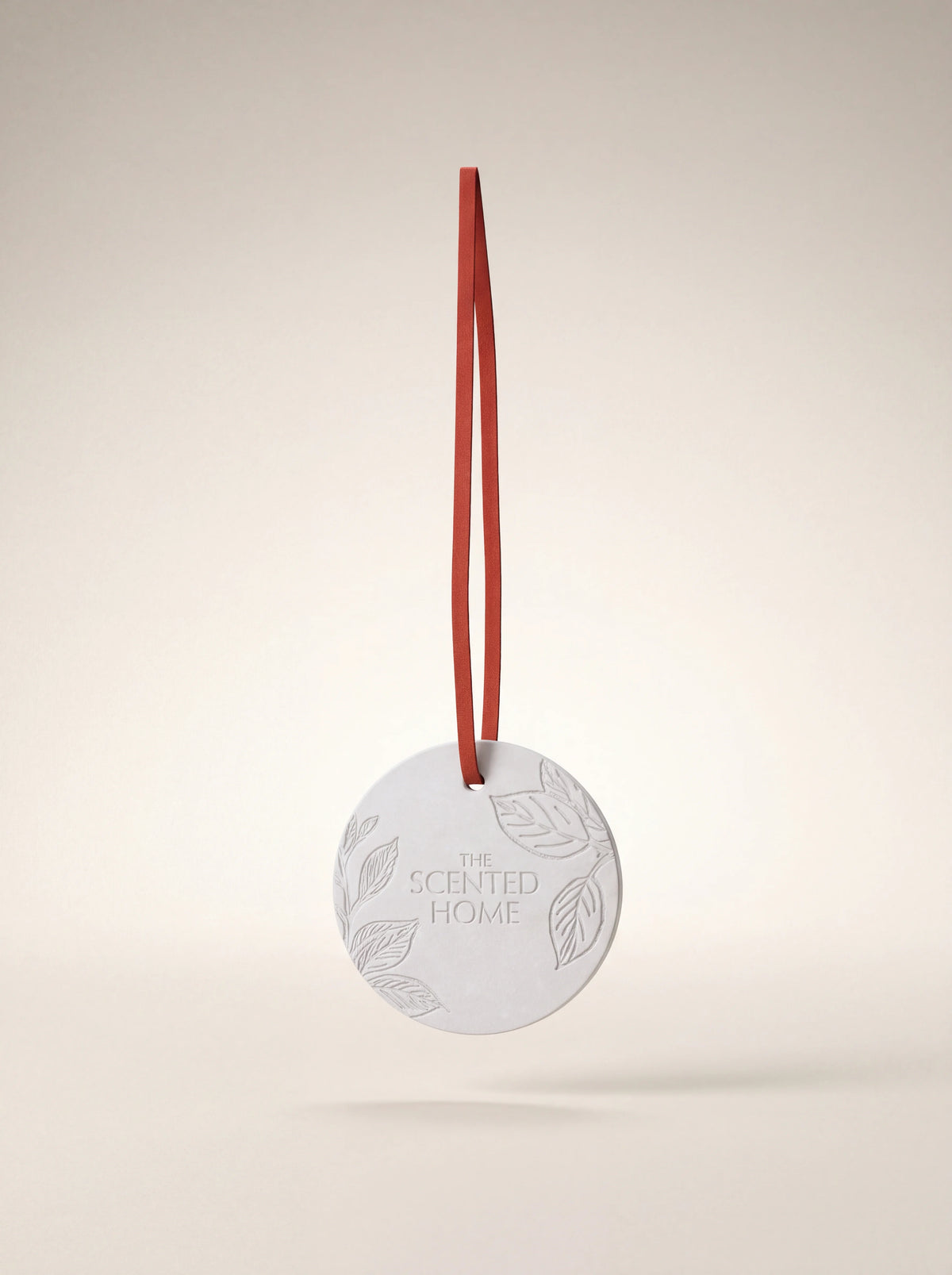 Embossed white ceramic diffuser disc suspended by a long red-orange hanging ribbon