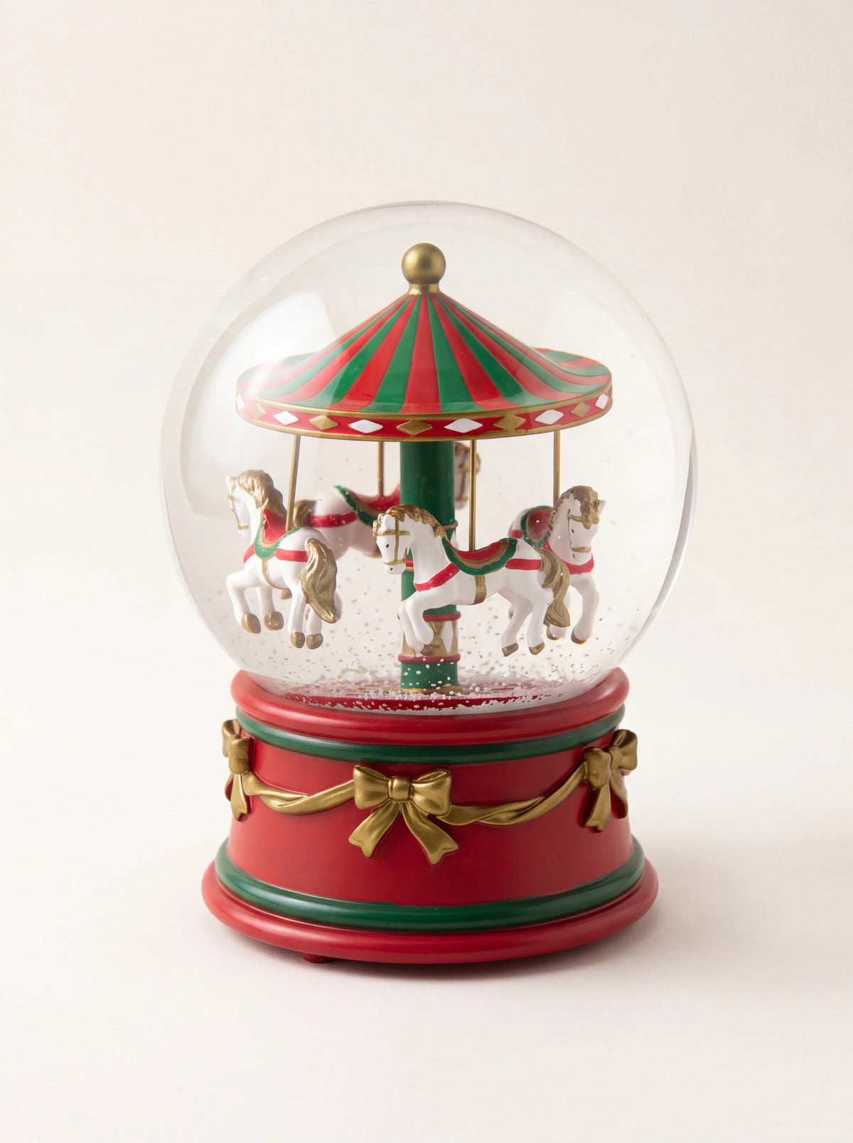 Carousel snow globe with white horses under a red and green striped canopy, on a red base with gold-tone bows
