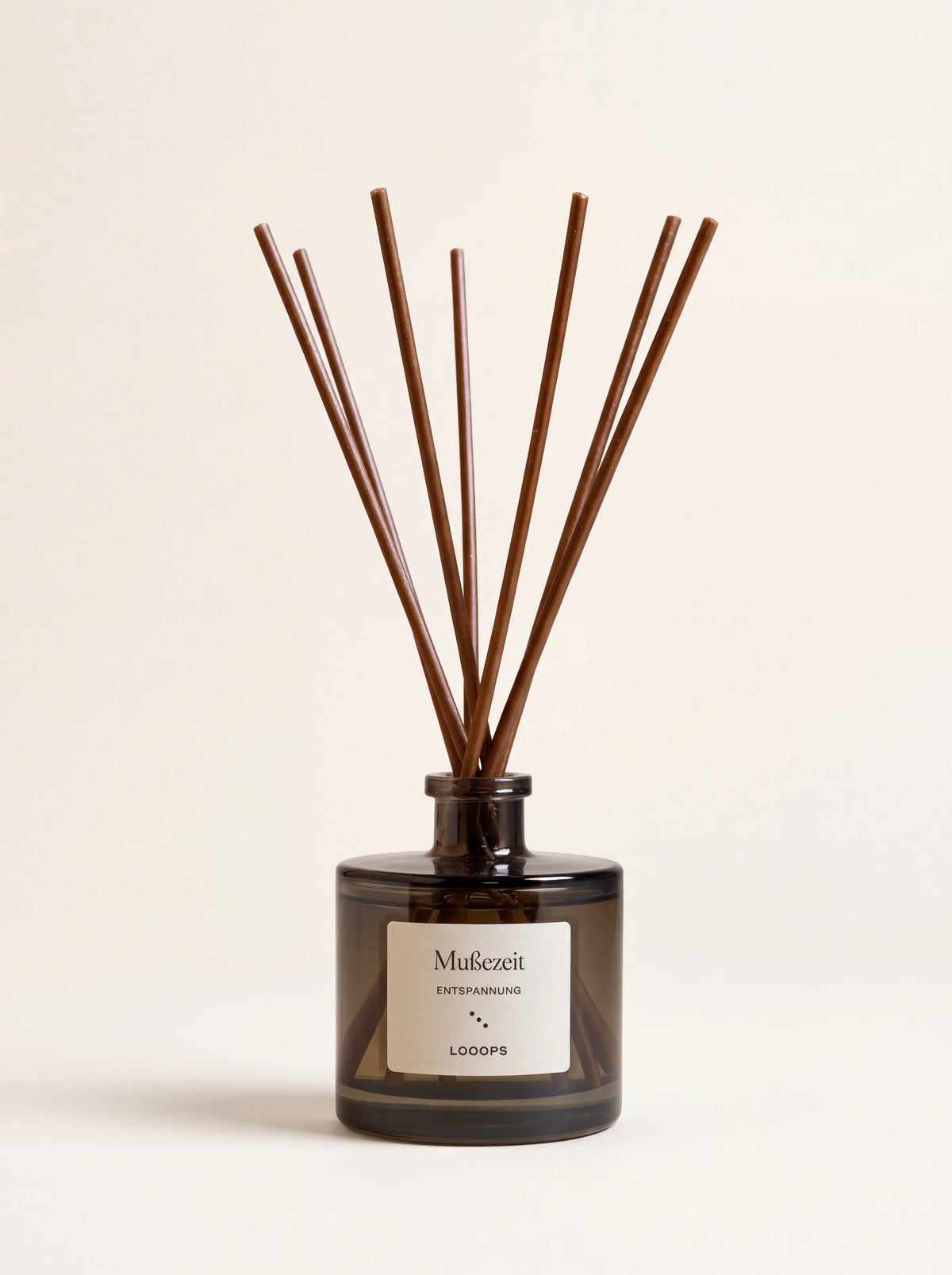 Cylindrical smoky brown glass reed diffuser with brown reeds and a label reading Mußezeit ENTSPANNUNG