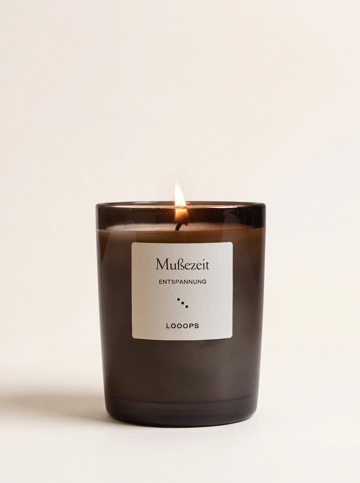 Lit scented candle in a dark glass jar with a white label reading Mußezeit ENTSPANNUNG LOOOPS
