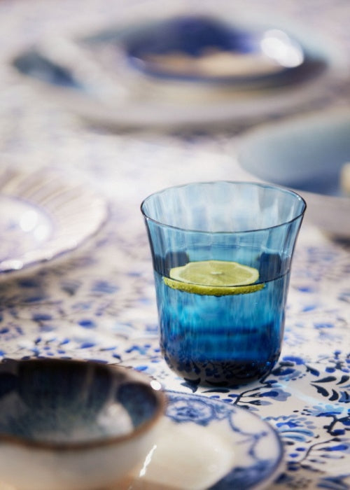 Blue fluted glass tumbler filled with water and a citrus slice on a patterned tablecloth