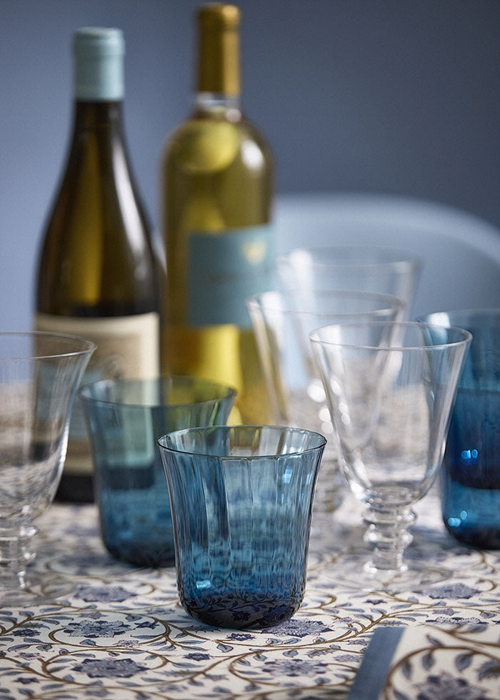 Blue glass tumblers arranged on a dining table with stemmed wine glasses and wine bottles