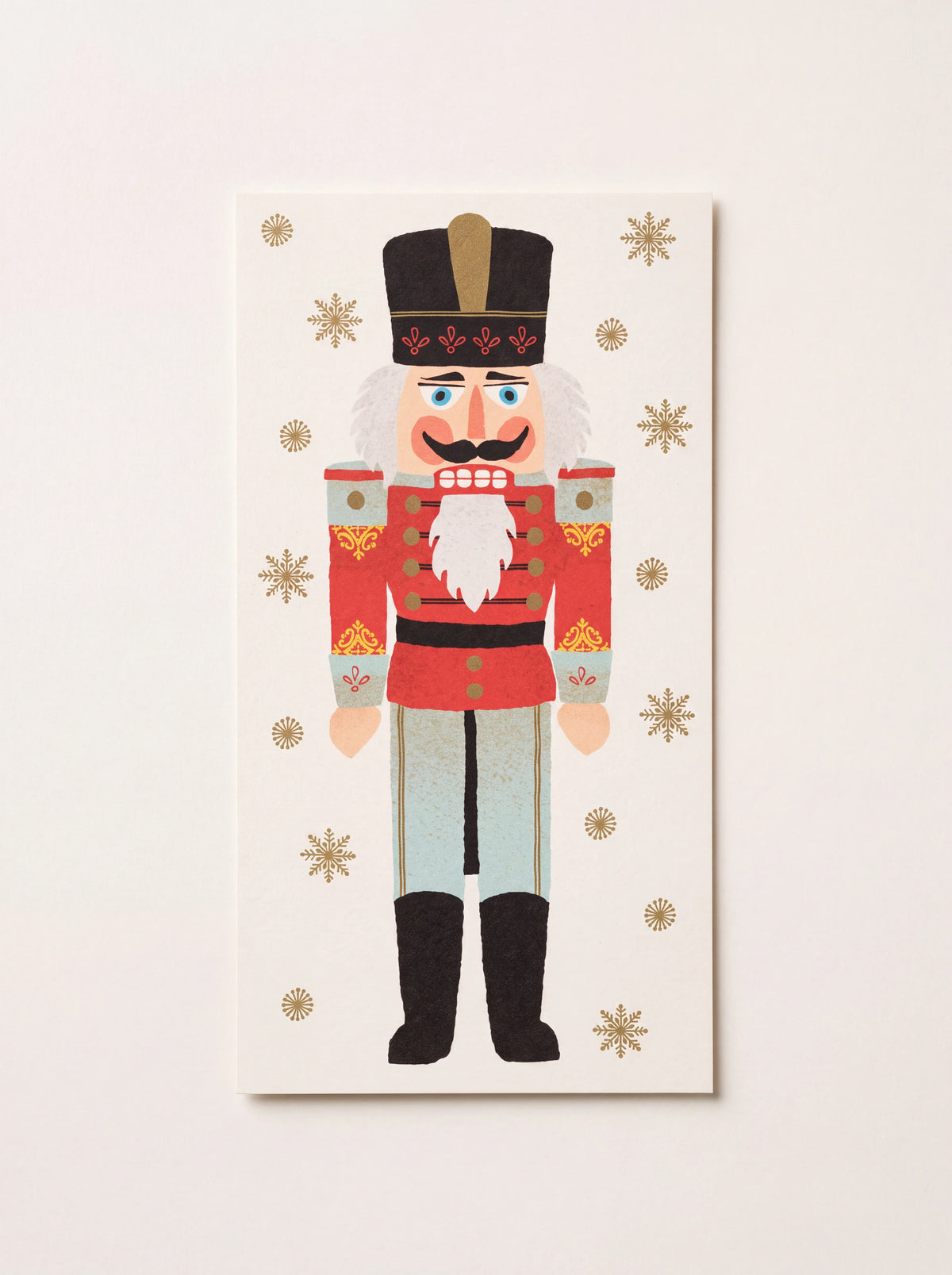 Rectangular paper guest napkin printed with a nutcracker soldier and gold snowflakes on a cream background