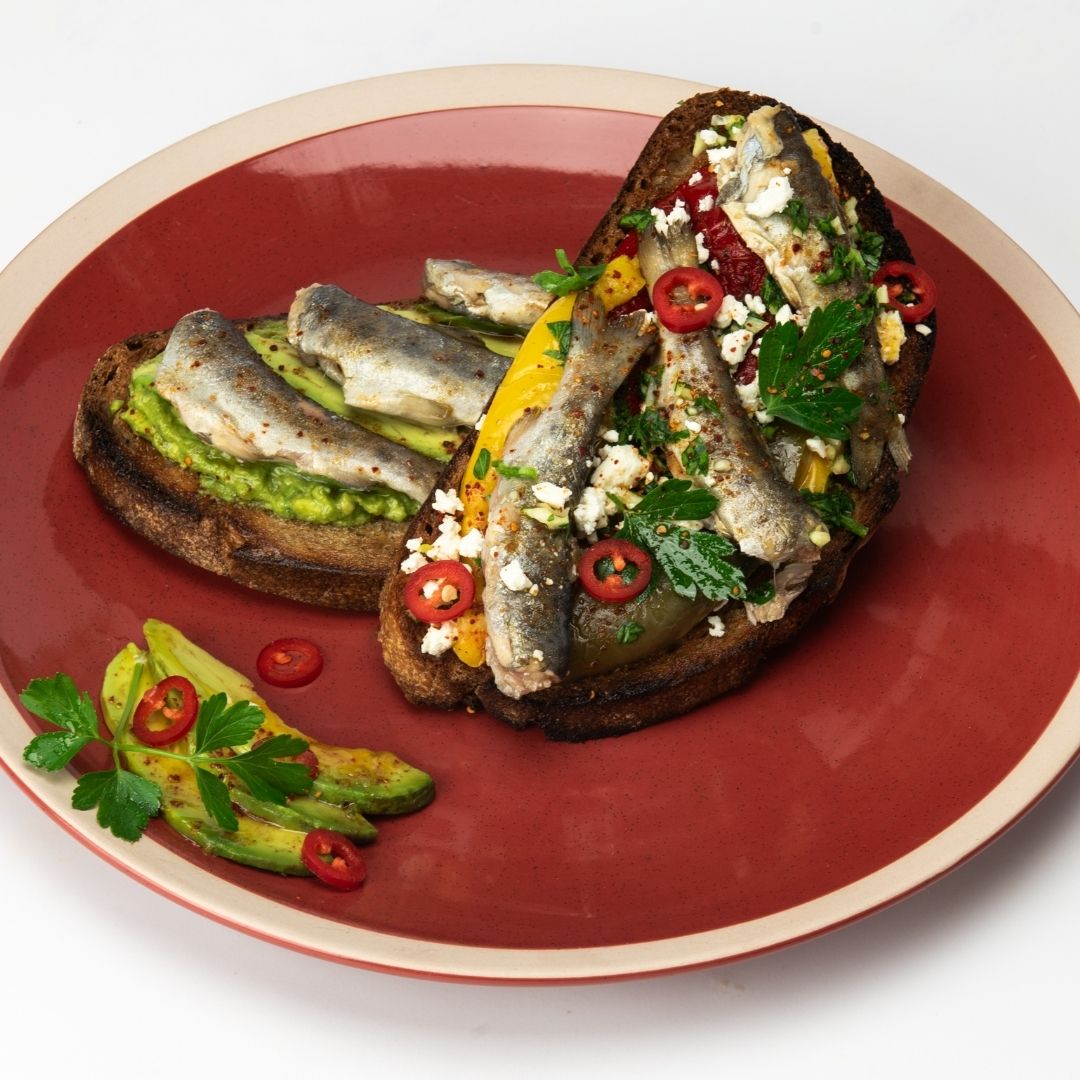Toasted bread topped with mountain trout, avocado, sliced red chilli and herbs on a red plate