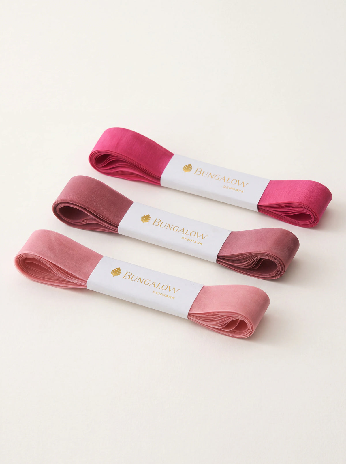 Set of three folded organza ribbons in fuchsia, mauve and pink, each secured with a paper band
