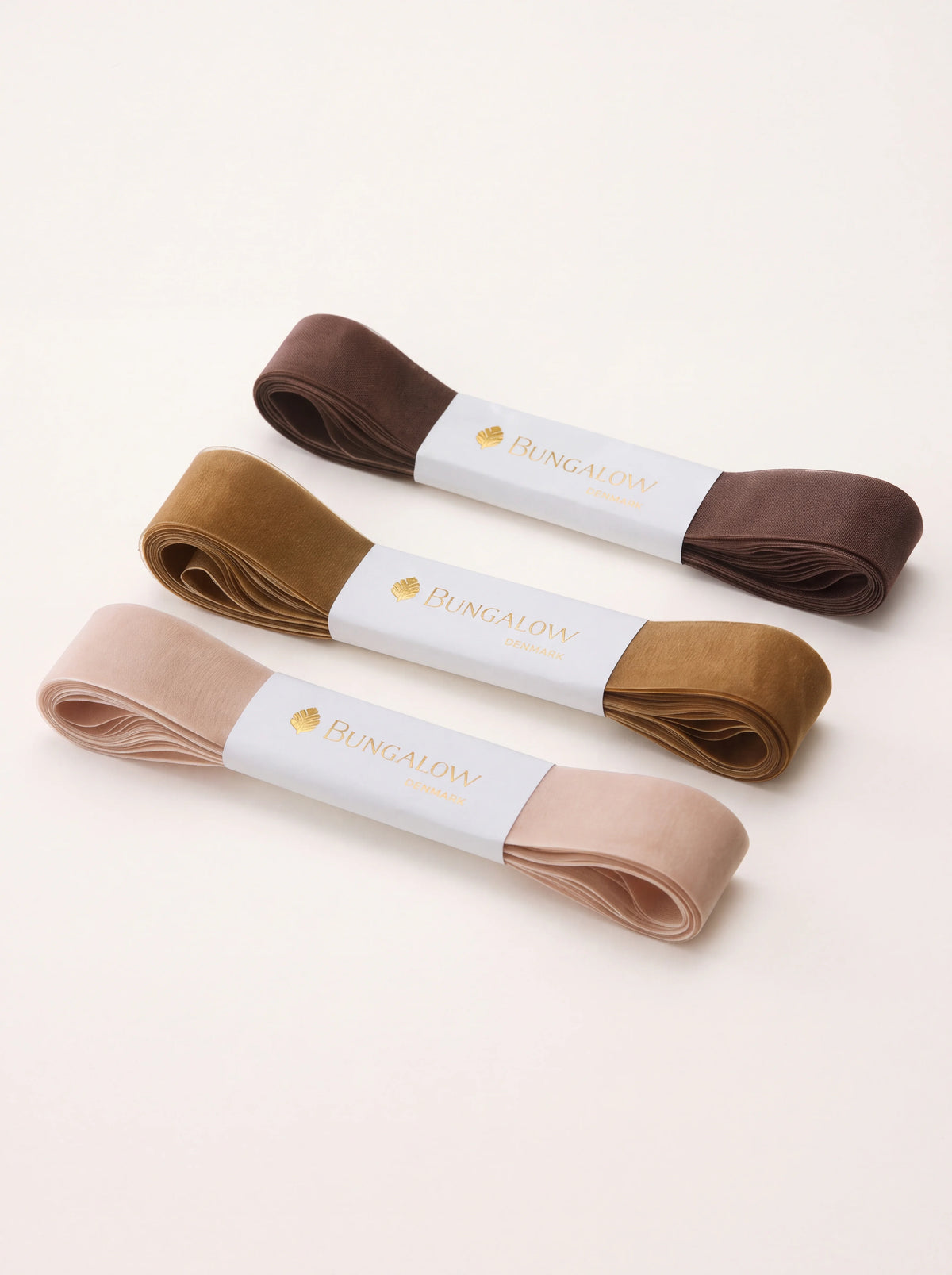 Set of three folded sheer organza ribbons in sand, ochre and dark brown, secured with white paper bands