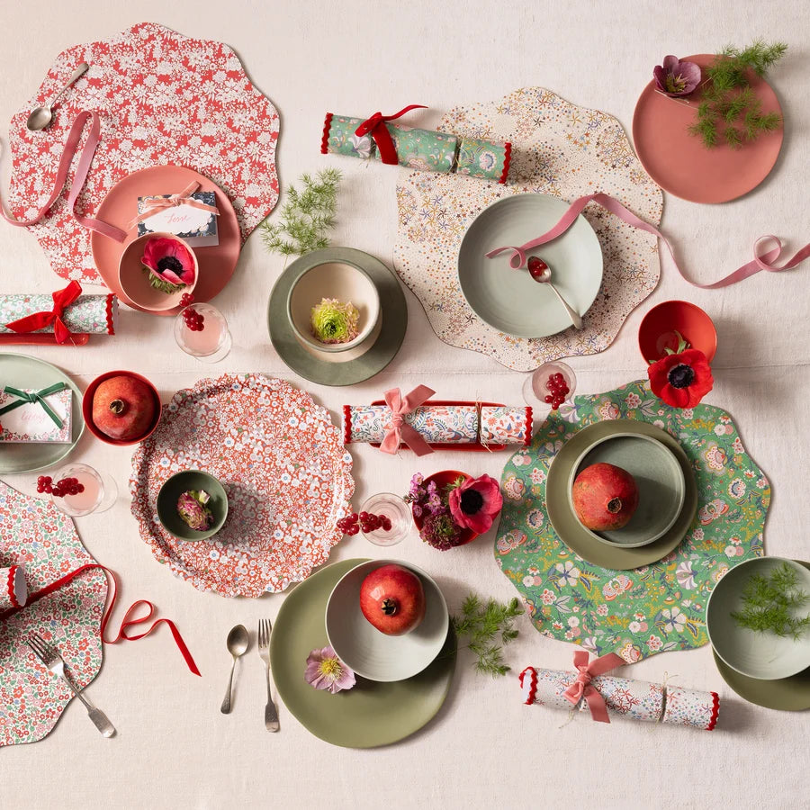 Paper crackers laid out across a festive dining table with floral placemats, ceramic plates and ribbon