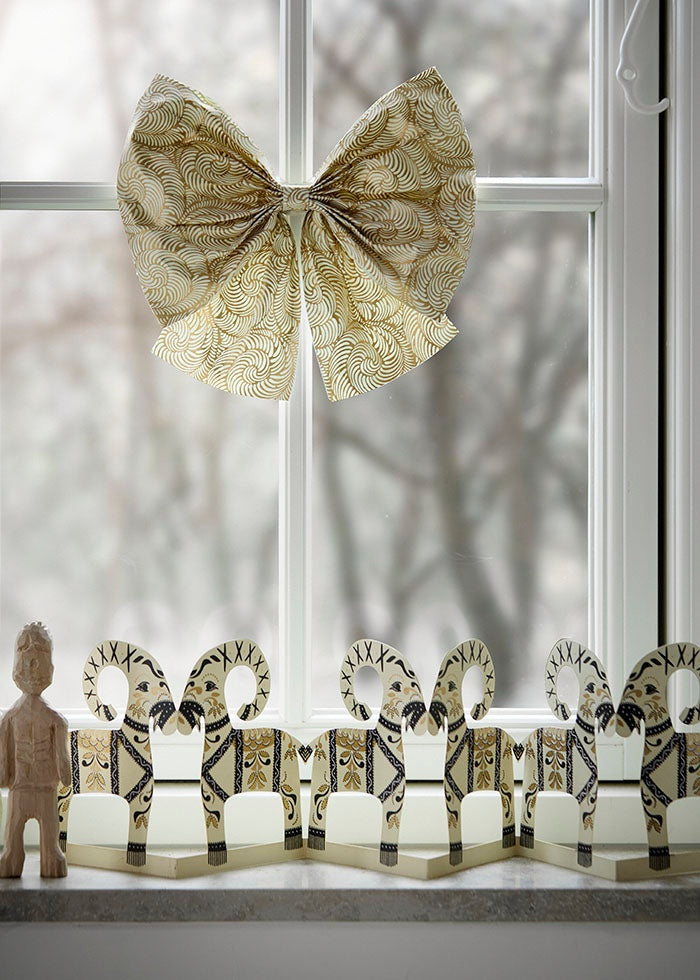Cream and gold paper bow displayed hanging on a white window frame