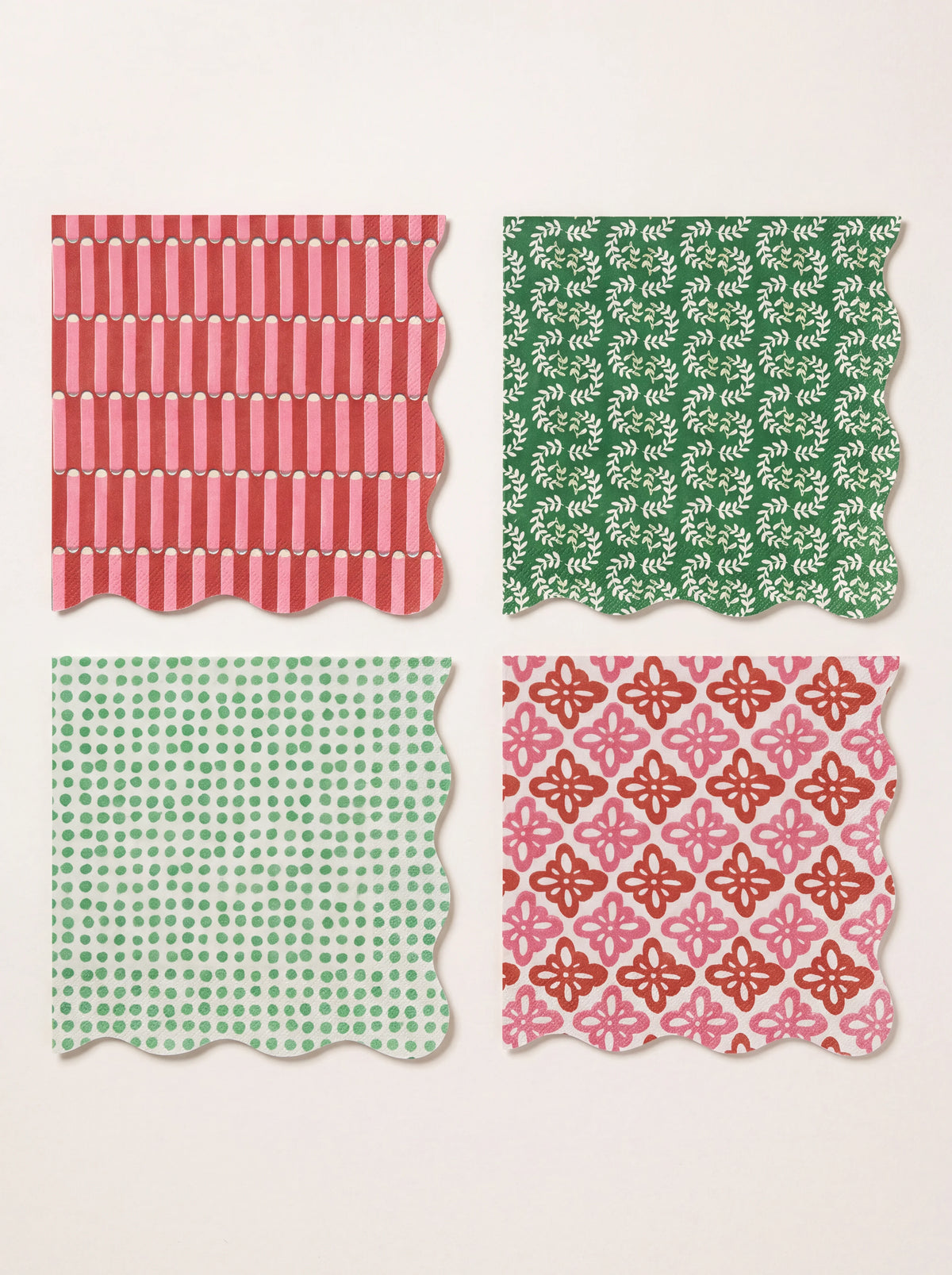 Four square scalloped paper napkins showing striped, floral, leaf and dot patterns in red, green and pink