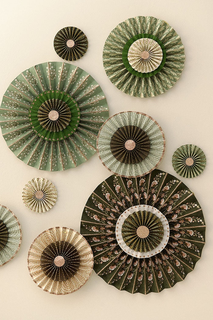 Olive paper rosette arranged on a wall alongside other pleated rosettes in assorted green patterns