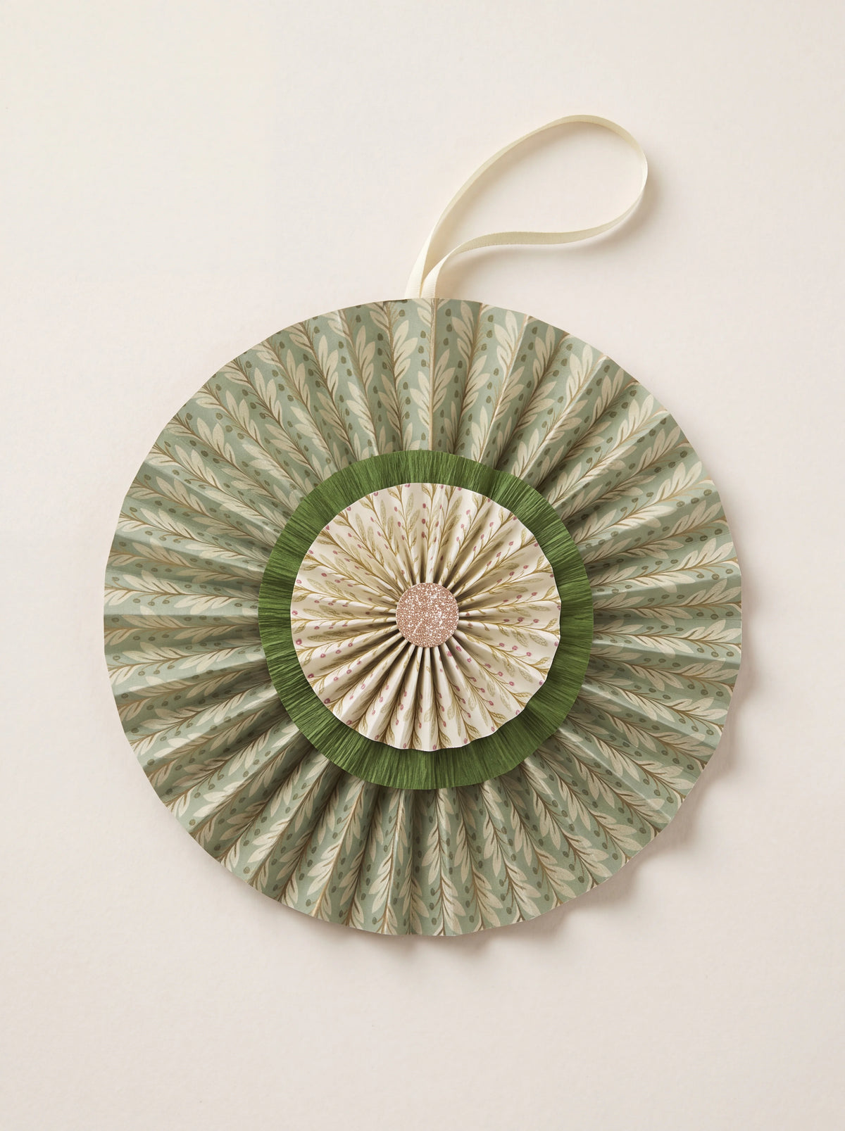 Pleated cotton paper rosette in sage green with three concentric tiers, a glitter centre and hanging ribbon