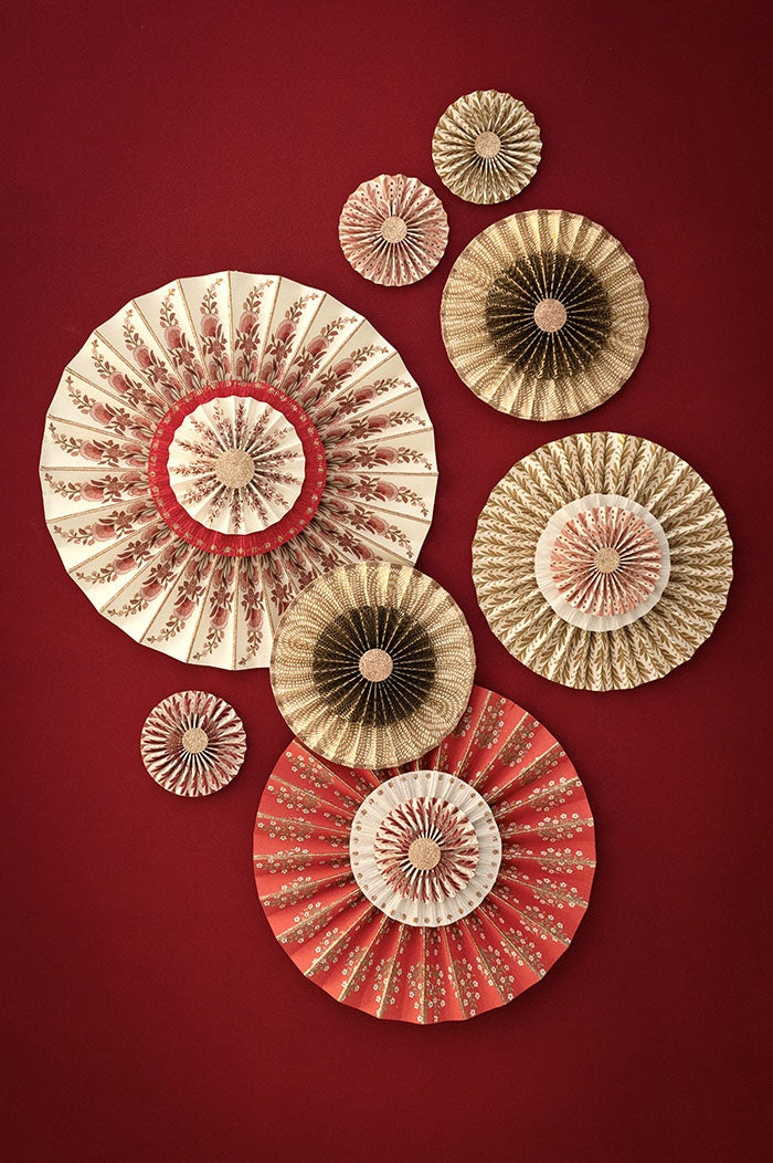 Scarlet paper rosette displayed among an arrangement of cream, gold, and red paper rosettes on a wall
