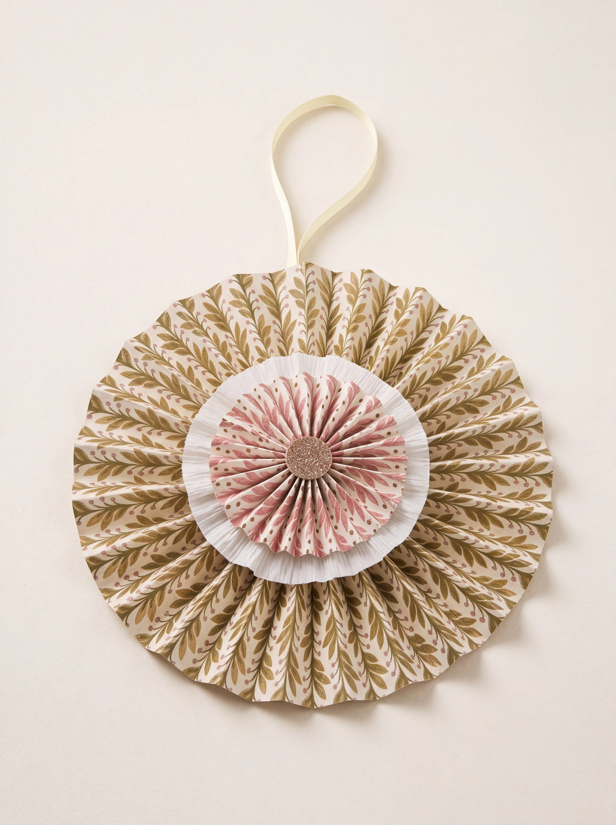 Pleated cotton paper rosette with layered botanical tiers, a central glitter disc and a hanging ribbon