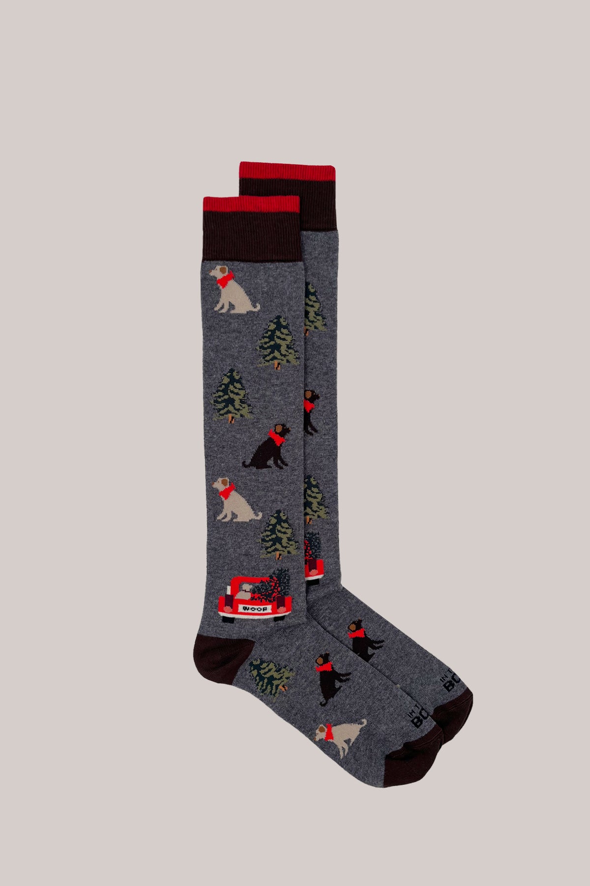 Grey knitted socks patterned with dogs and pine trees, featuring dark brown heels, toes and red-trimmed cuffs