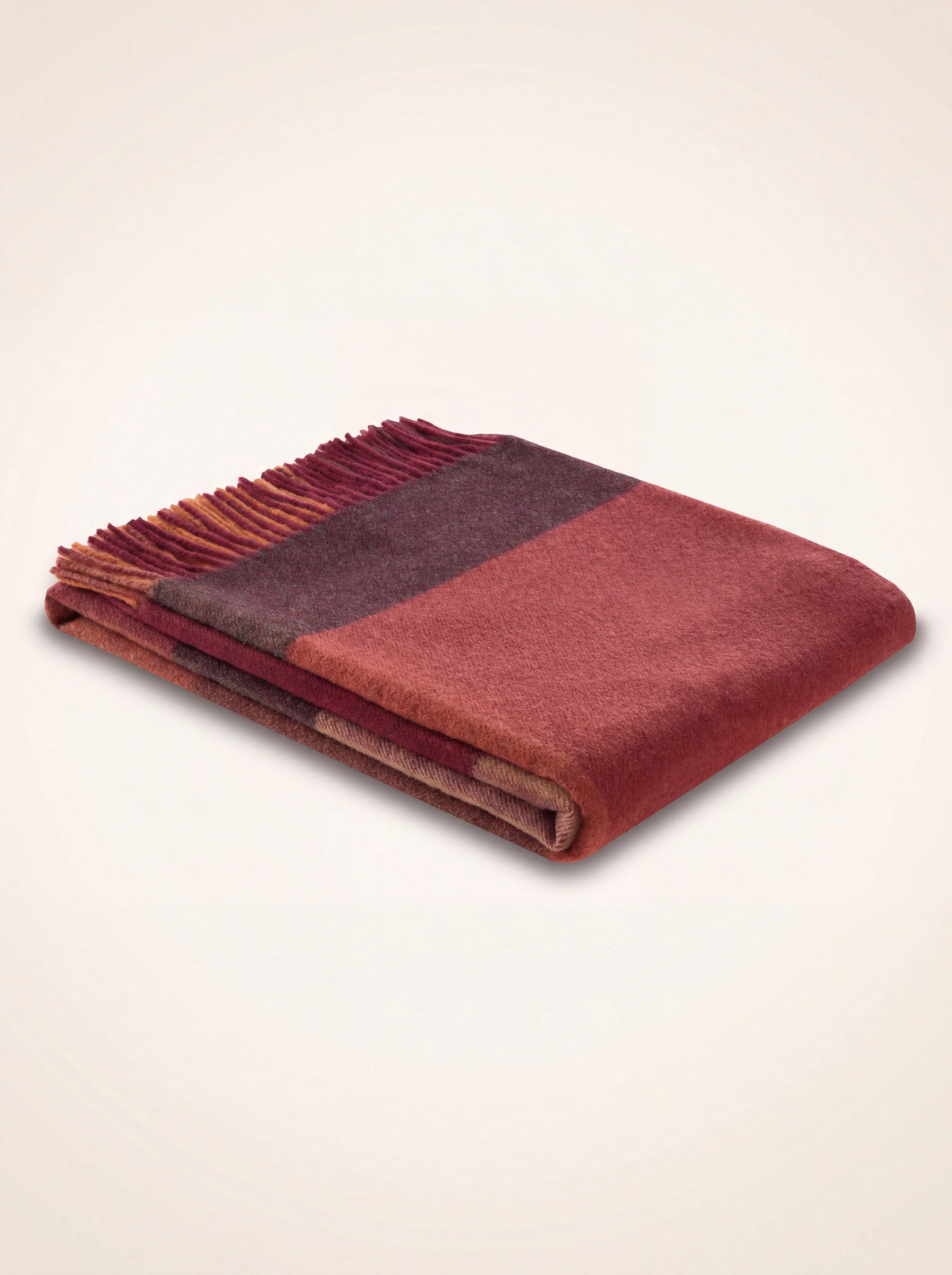 Wool and cashmere blanket folded flat, showing red and burgundy colour blocks and fringed trim