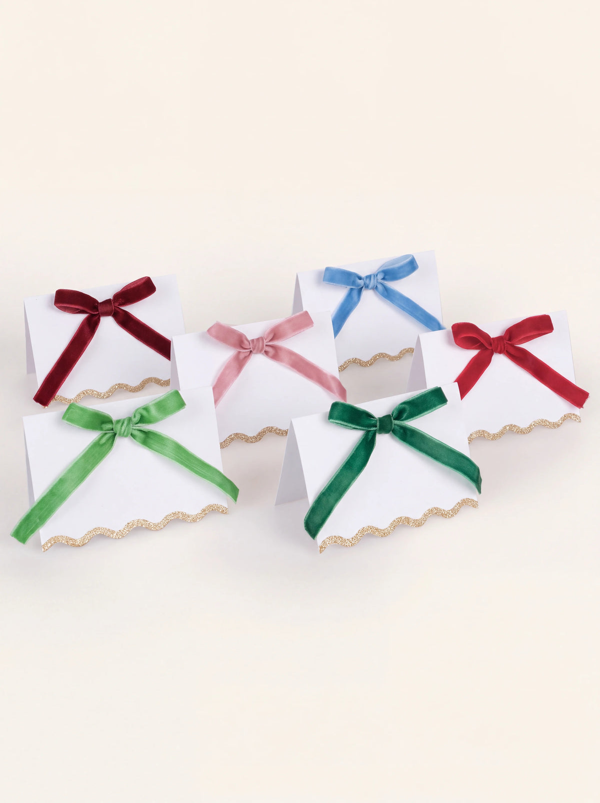 Set of six white paper place cards with scalloped gold glitter edges and velvet bows in assorted colours