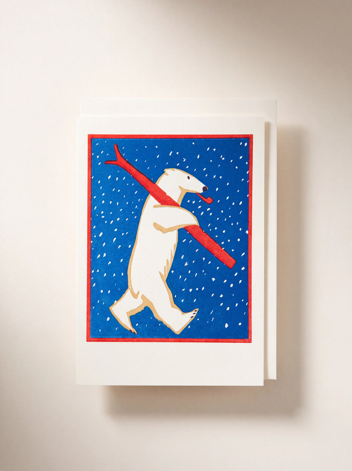 Greeting card illustrated with a polar bear carrying a red ski and pipe against a snowy blue background