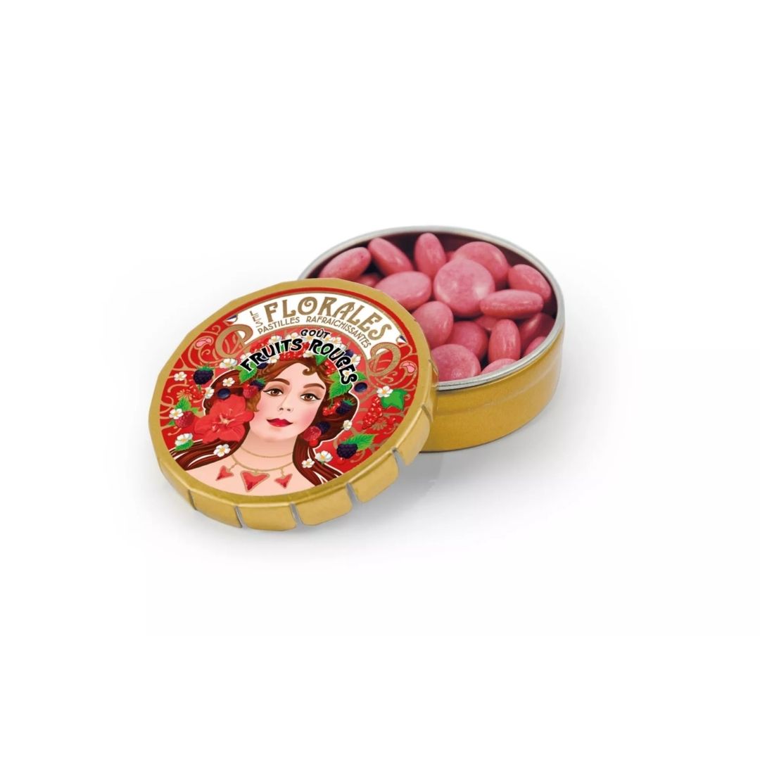 Open gold-tone tin revealing small pink pastilles inside, with the illustrated lid leaning in front