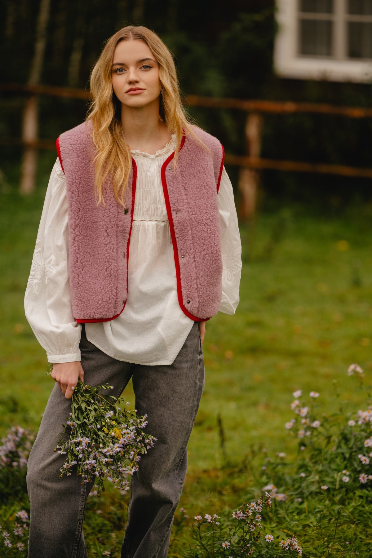 Pink wool vest worn unbuttoned, showing the straight cut and red trim along the opening