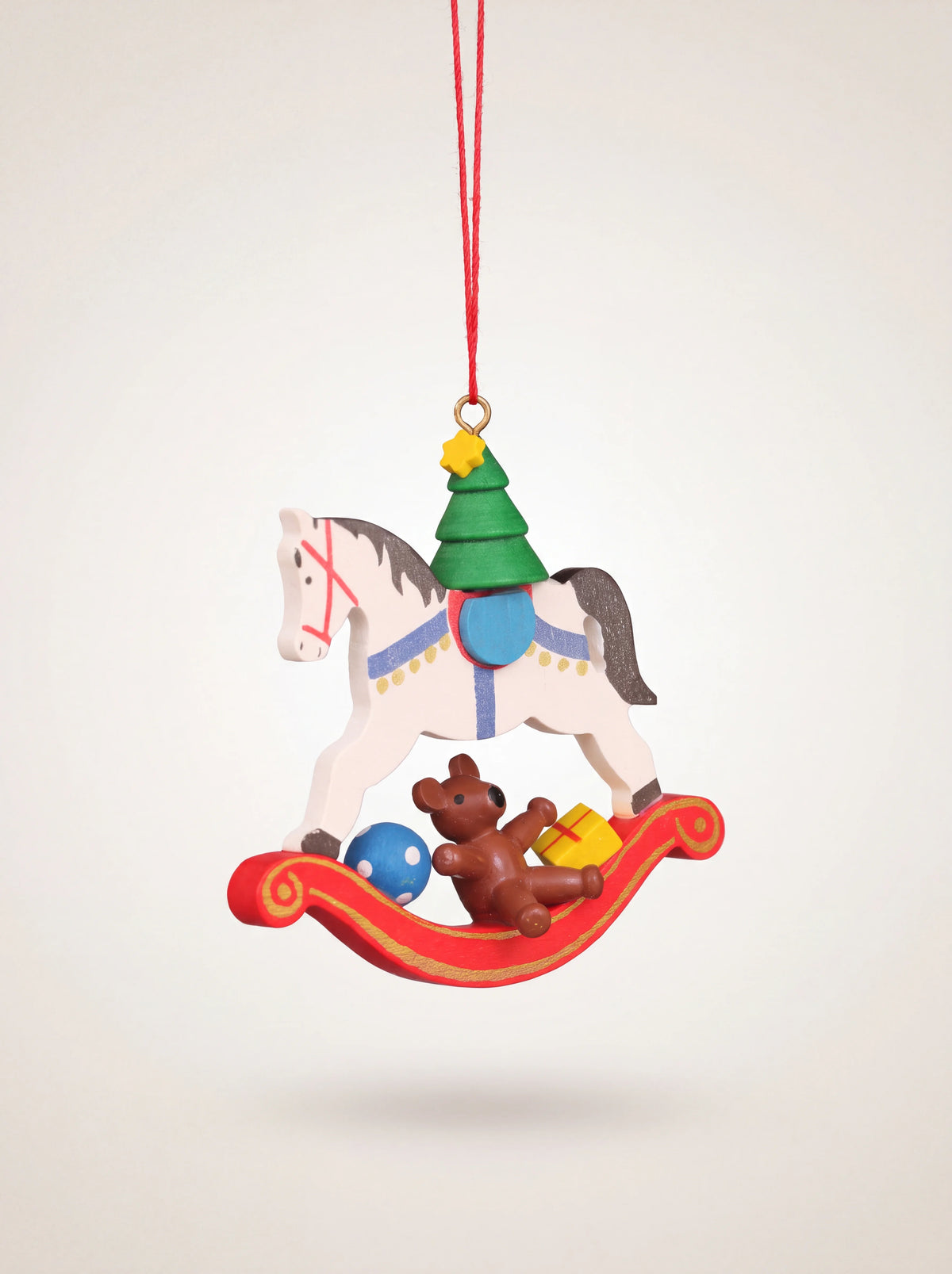 Painted wooden rocking horse ornament with a red rocker, miniature Christmas tree, and brown teddy bear