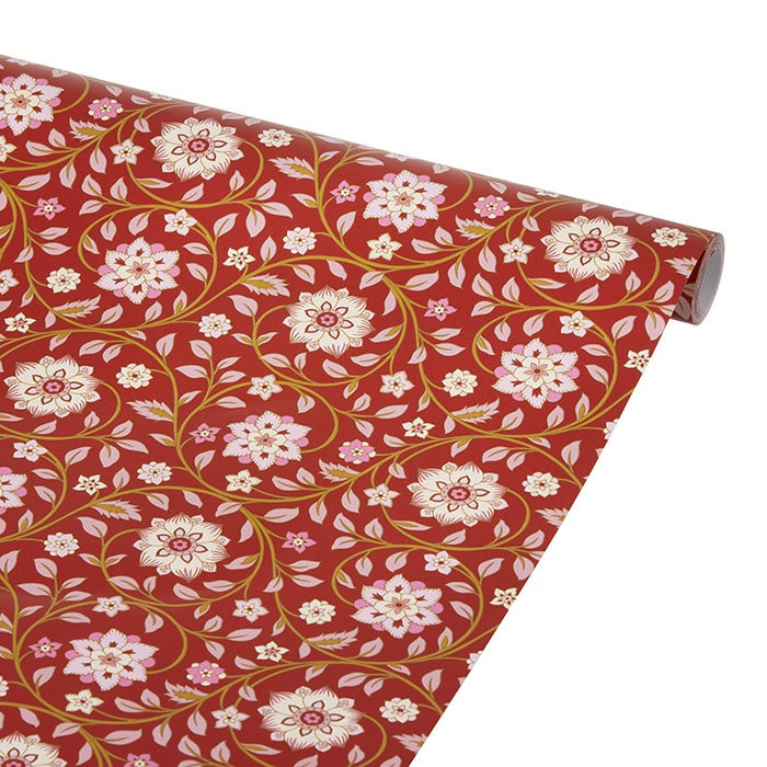 Roll of scarlet red wrapping paper unrolled to show a floral vine pattern in pink, white, and gold