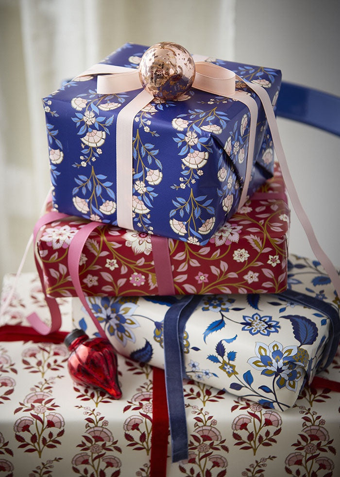 Gift parcel wrapped in the scarlet floral paper and tied with pink ribbon, in a stack of presents