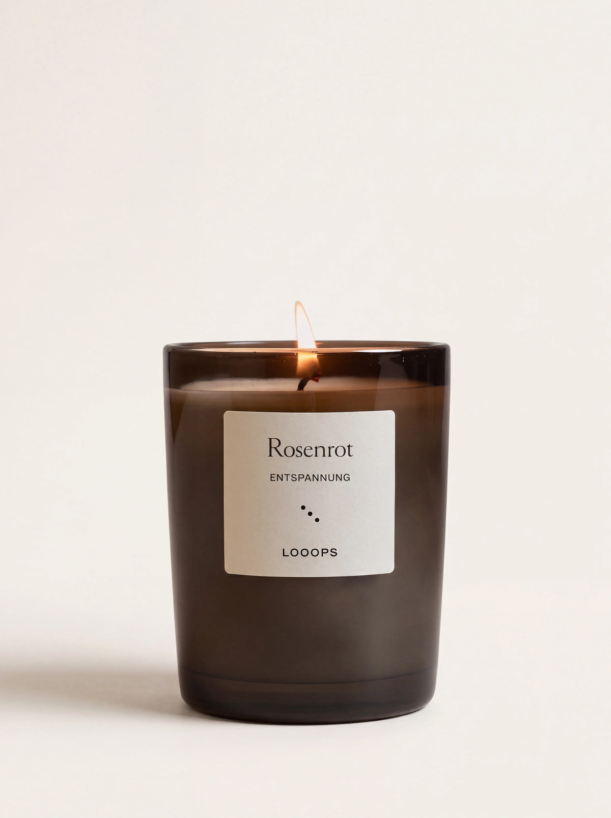 Lit scented candle in a dark tinted glass jar with a label reading Rosenrot ENTSPANNUNG LOOOPS