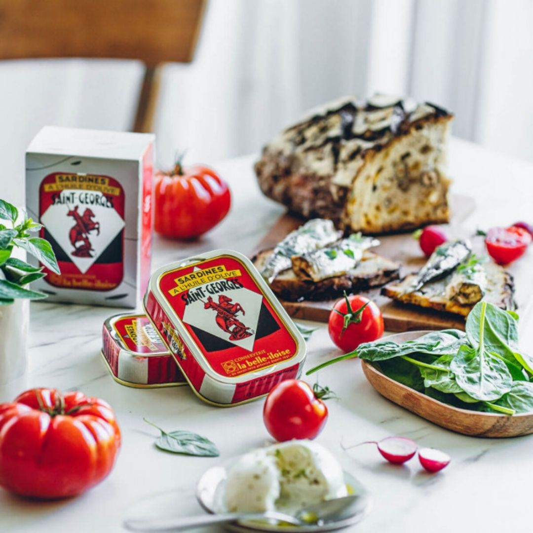Sardine tins and outer box displayed with sardines served on crusty bread with tomatoes