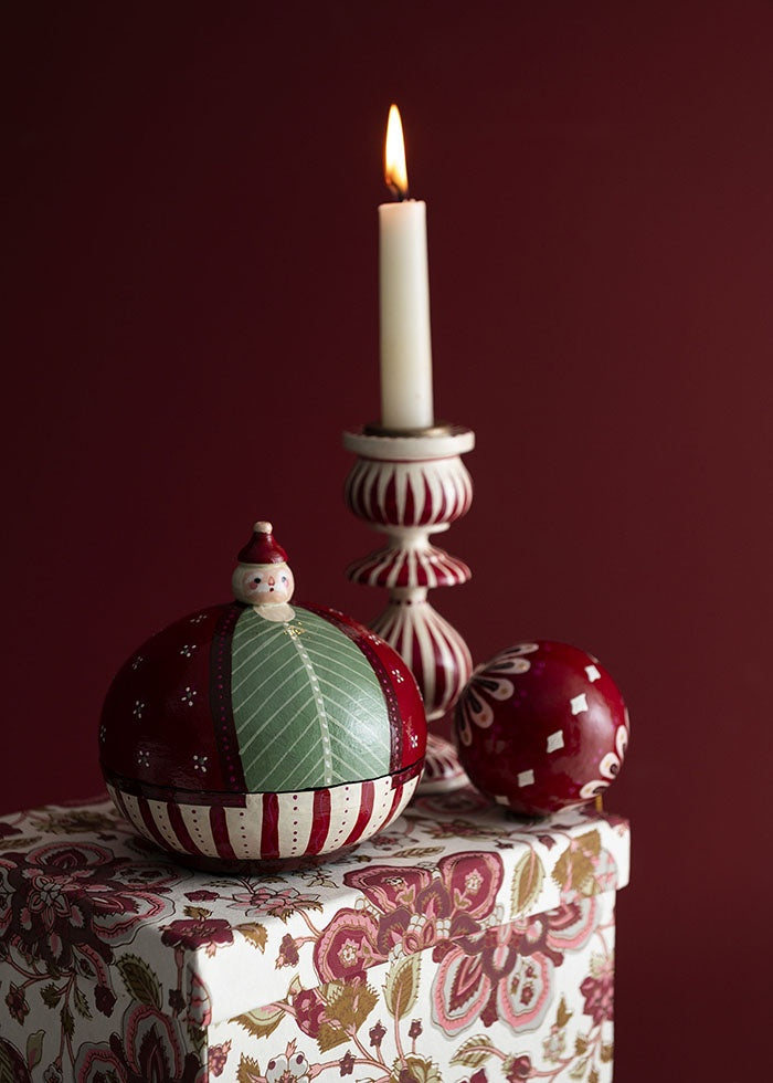 Santa paper mâché box styled beside a lit candlestick and painted round bauble