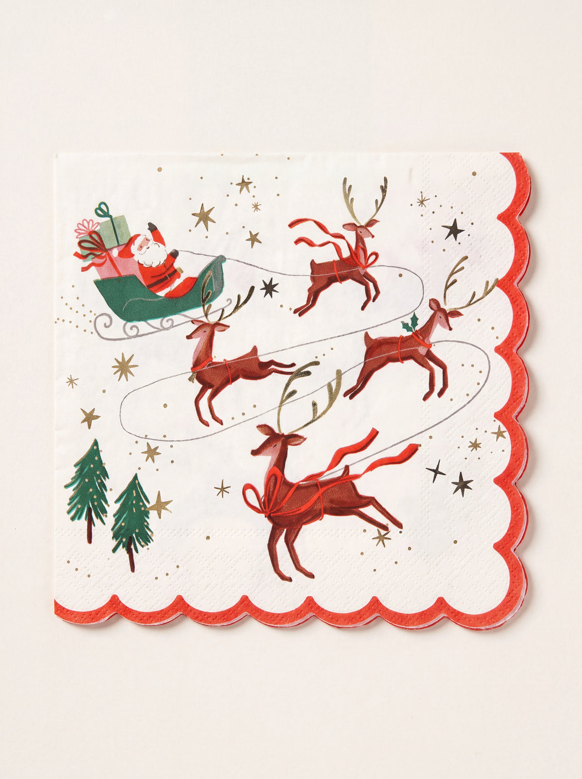 Square white paper napkin with a red scalloped border, illustrated with Santa in a sleigh pulled by reindeer