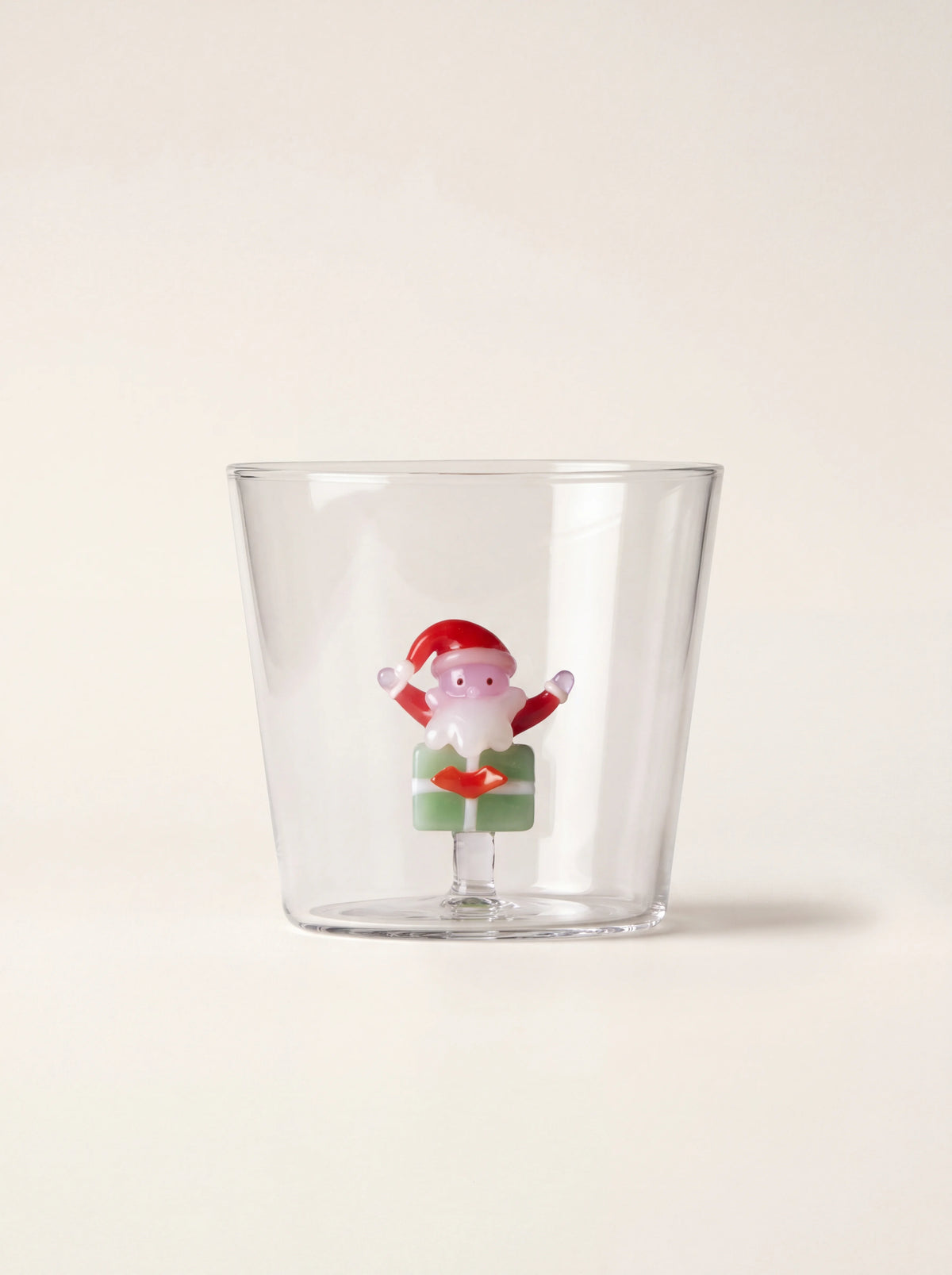 Clear glass tumbler with an internal glass Santa Claus figurine perched on a green gift box