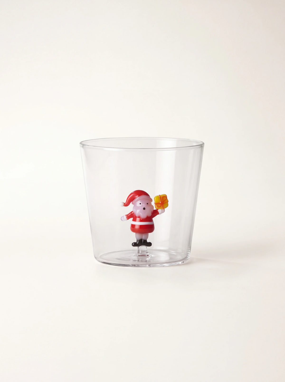 Clear glass tumbler with a miniature Santa Claus figure holding a yellow gift inside the base
