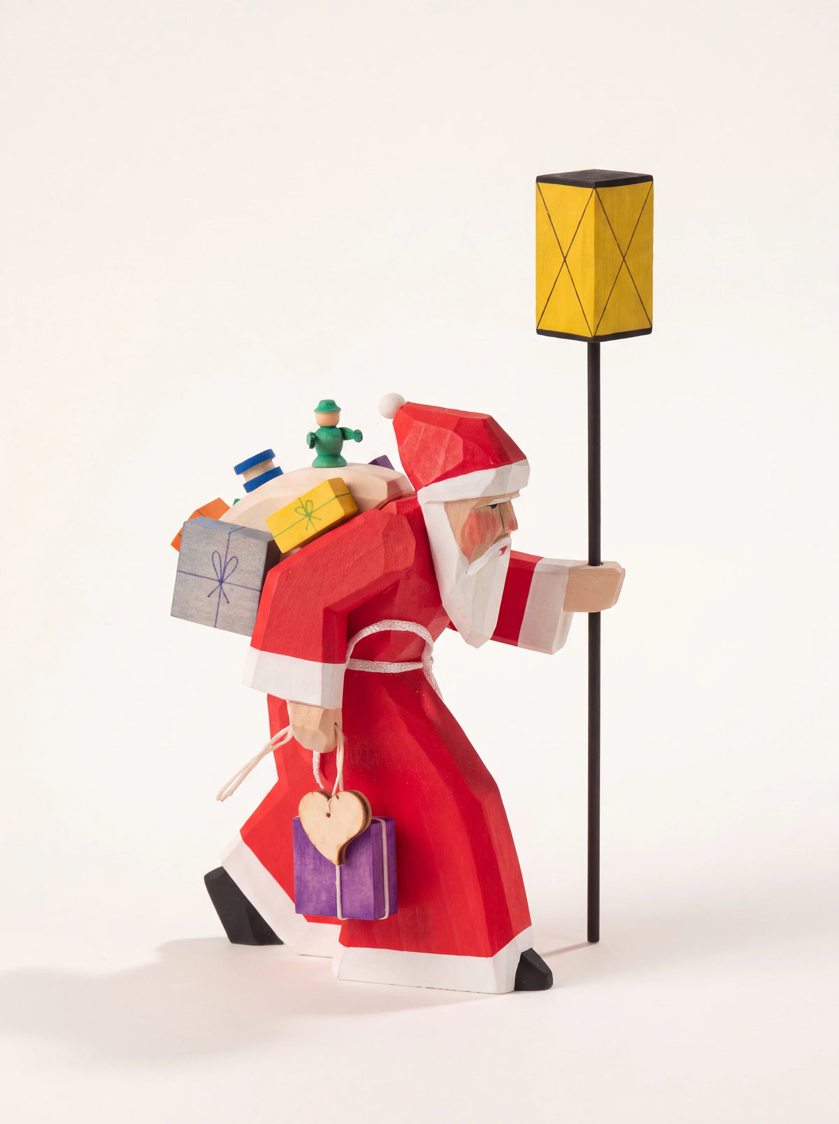 Carved wooden Santa figurine carrying a sack of gifts and holding a tall yellow lantern