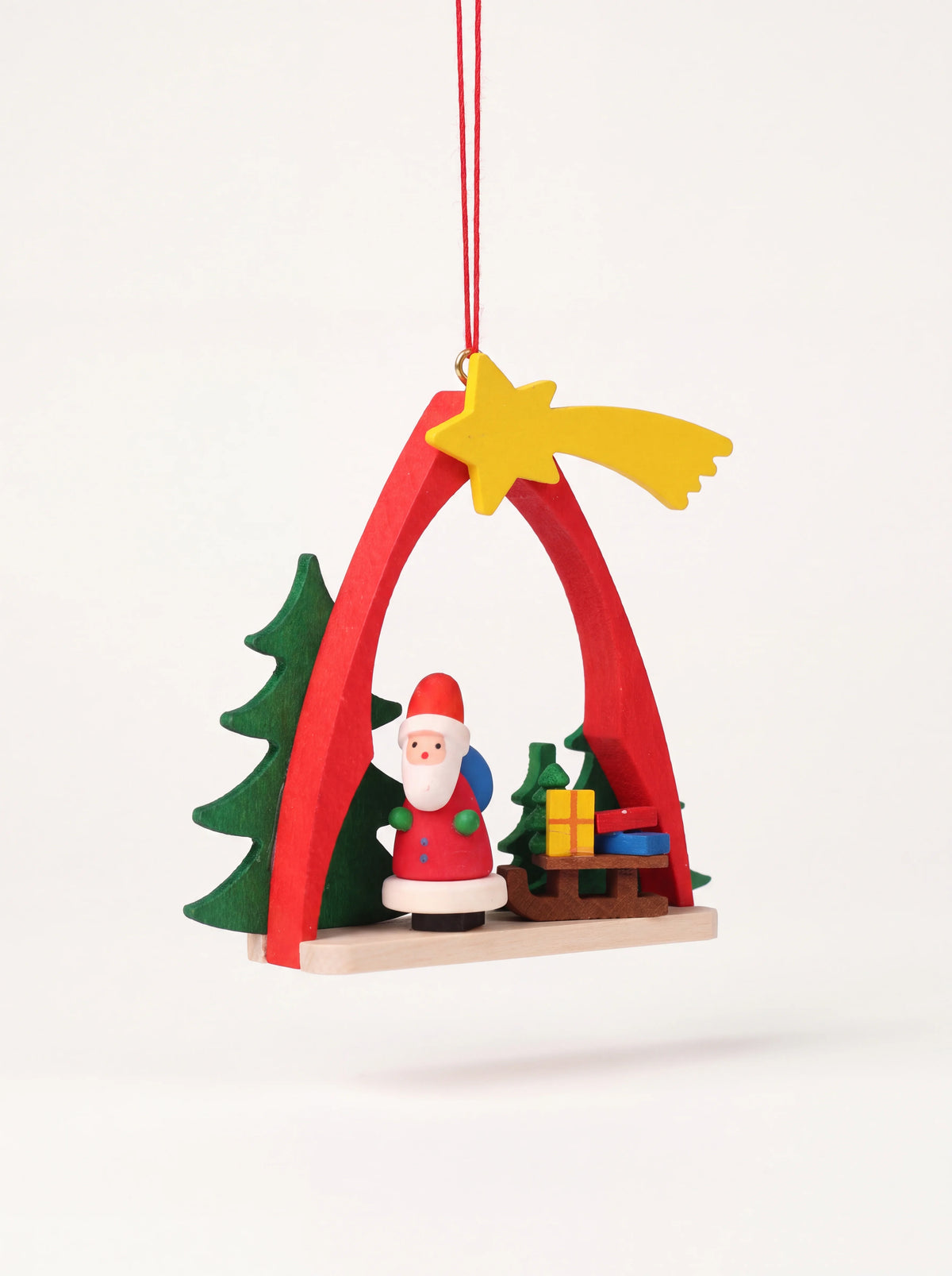 Wooden Santa Christmas ornament with a red arch, shooting star, evergreen trees and a sledge with presents