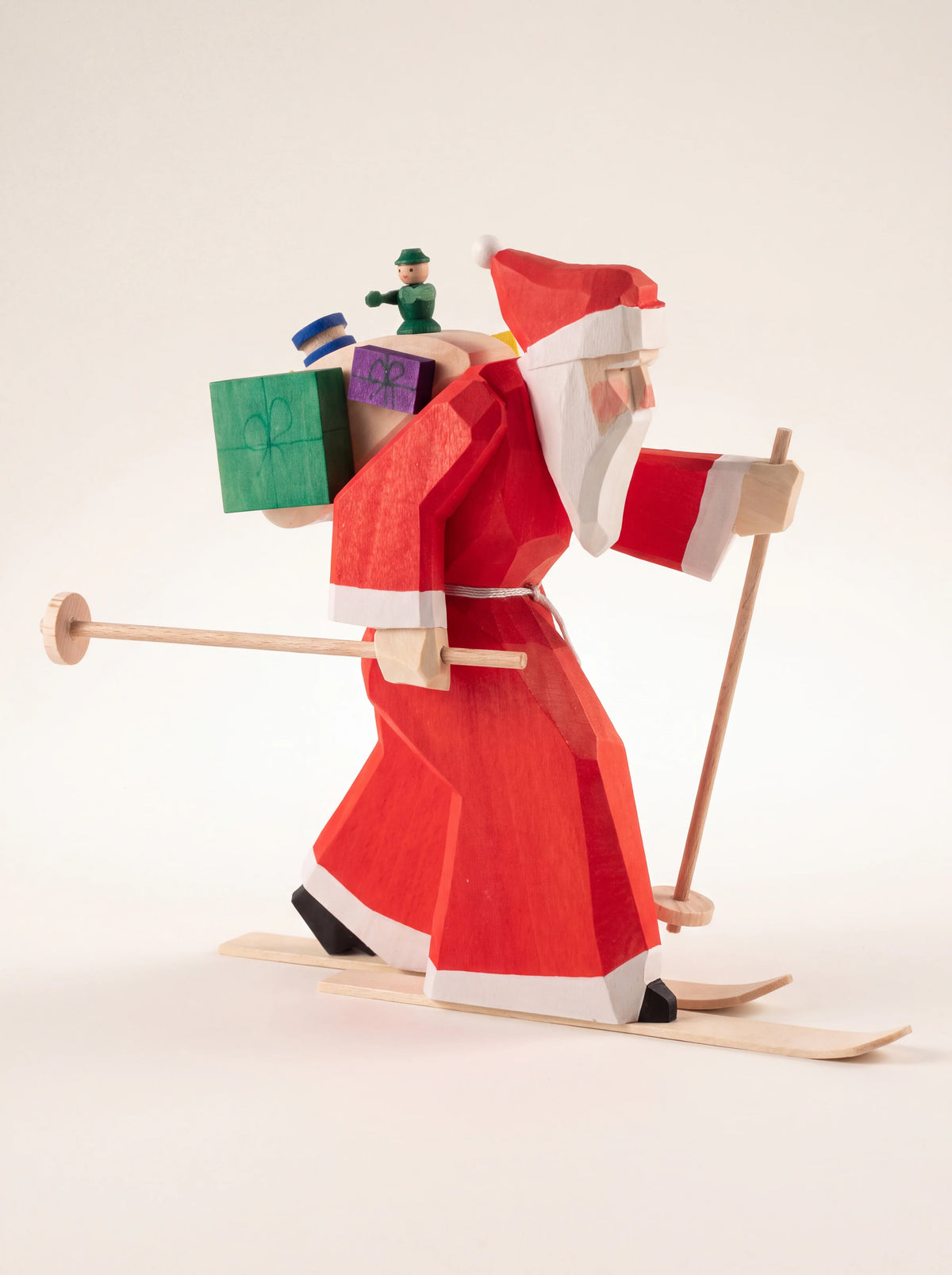 Carved wooden Santa figurine on skis with poles, wearing a red coat and carrying a sack of gifts